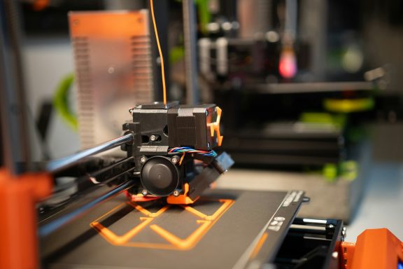 3D-Drucker, der ein oranges Muster auf einer schwarzen Druckplatte erstellt.