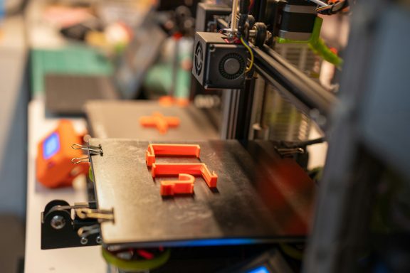 3D-Drucker mit orangefarbenen Teilen auf der Druckplatte.