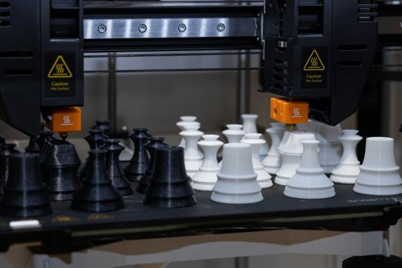 Schachfiguren in Schwarz und Weiß, teilweise im 3D-Druckprozess.