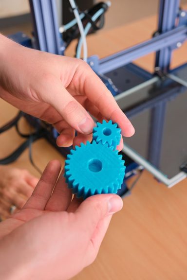 Zwei blaue Zahnräder aus einem 3D-Drucker in der Hand gehalten.