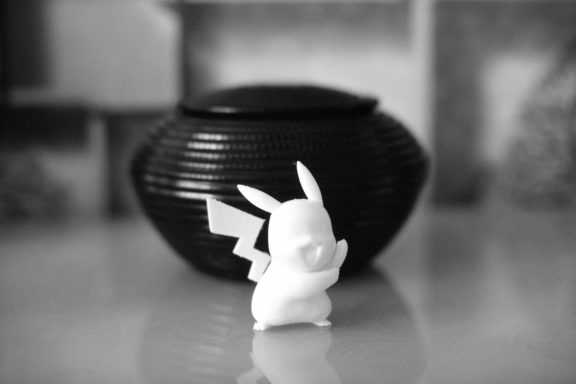 Ein kleiner Pikachu-Charakter steht vor einem schwarzen, runden Behälter.